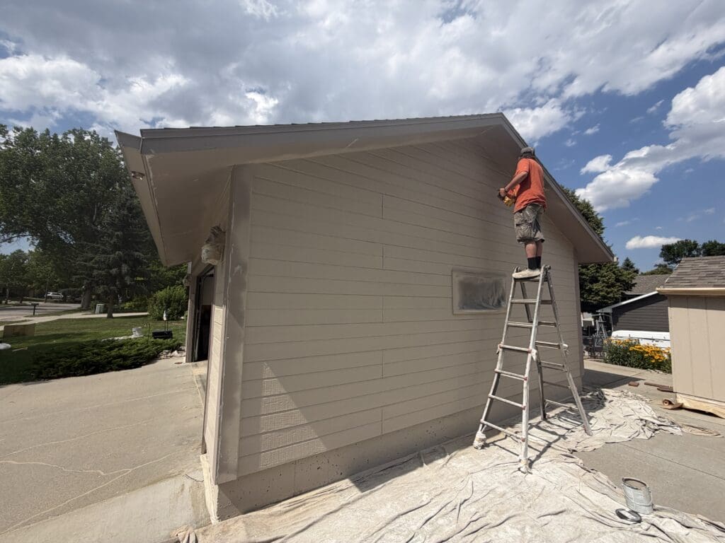 Professional painter applying exterior paint to a home's siding during an exterior house painting project in Rapid City, South Dakota.