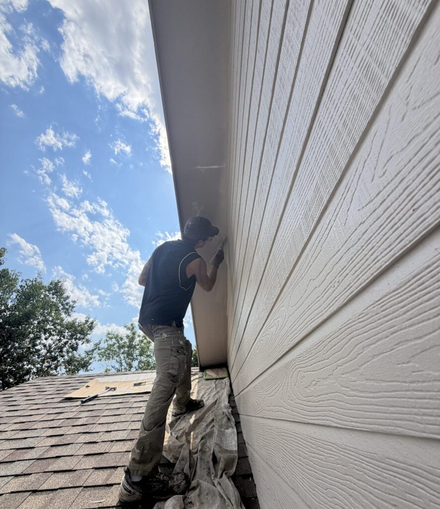 Exterior house painter carefully painting soffits and fiber cement siding on a residential home in Rapid City, South Dakota.