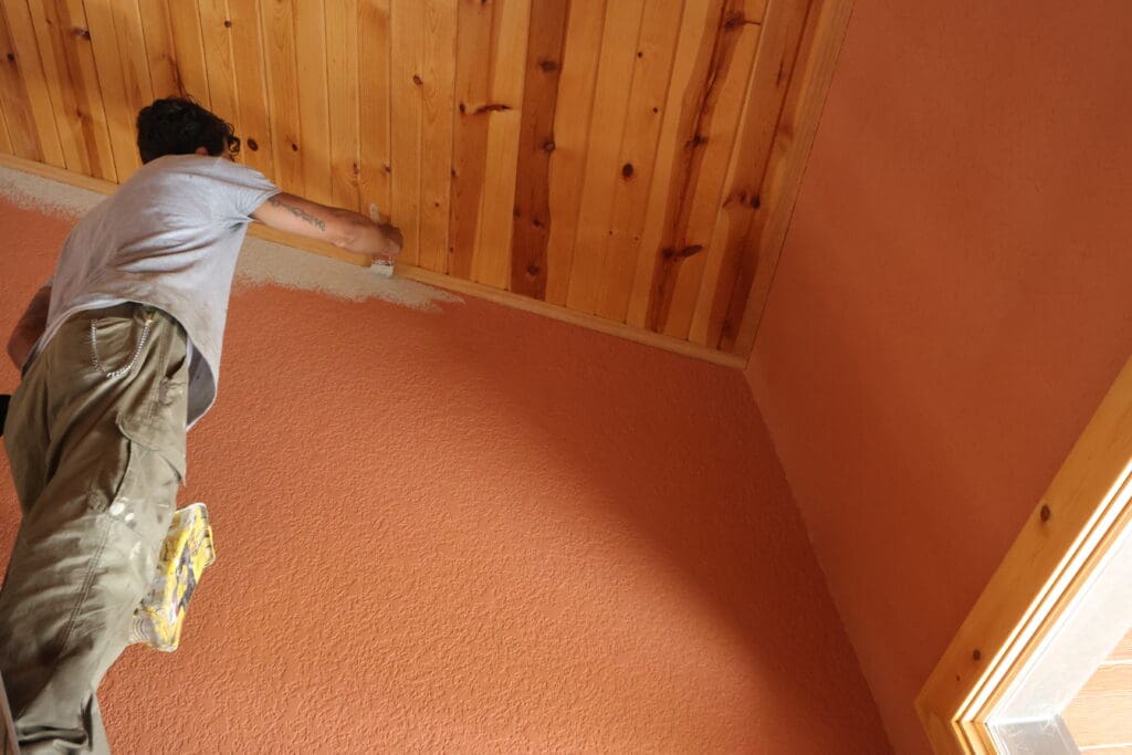 Professional painter cutting in textured interior walls around a tongue-and-groove wood ceiling during a residential interior painting project in the Black Hills, South Dakota.