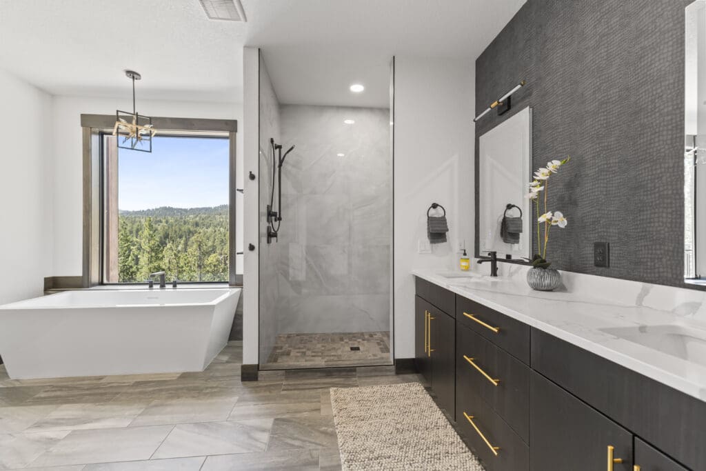 Bathroom with textured charcoal wallpaper behind a double vanity, a freestanding tub, and a forest-view window in a Powder House Pass home near Lead, SD.
