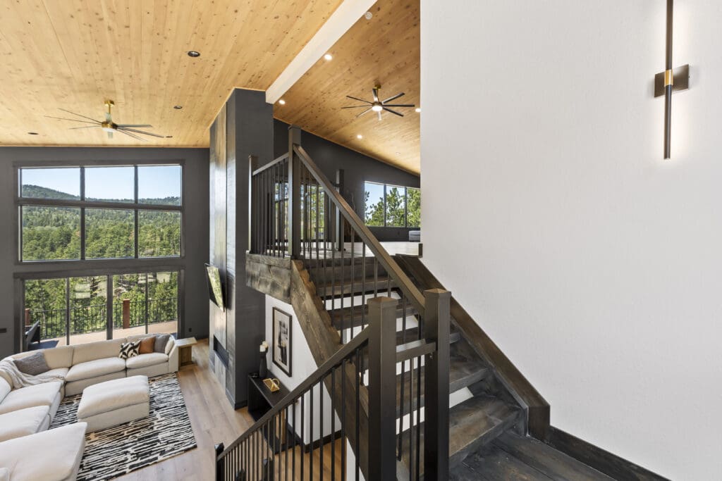 Open staircase with dark-stained wood treads and railings beside a tall white stairwell wall, overlooking the great room in a Powder House Pass home near Lead, SD.