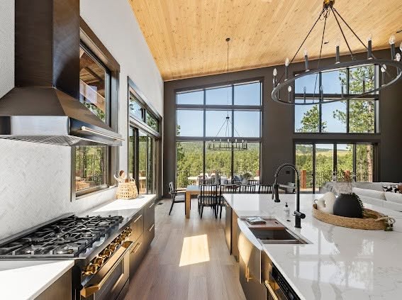 Kitchen with white walls, a black range hood, and a quartz island opening to a dining area with tall windows in a Powder House Pass home near Lead, SD.