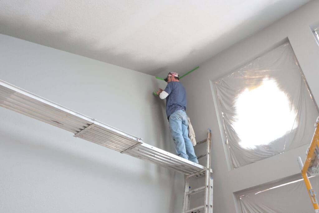 Black Mountain Painting painter on a plank taping the ceiling line in a new construction home in Flatland Estates, Aberdeen, SD.